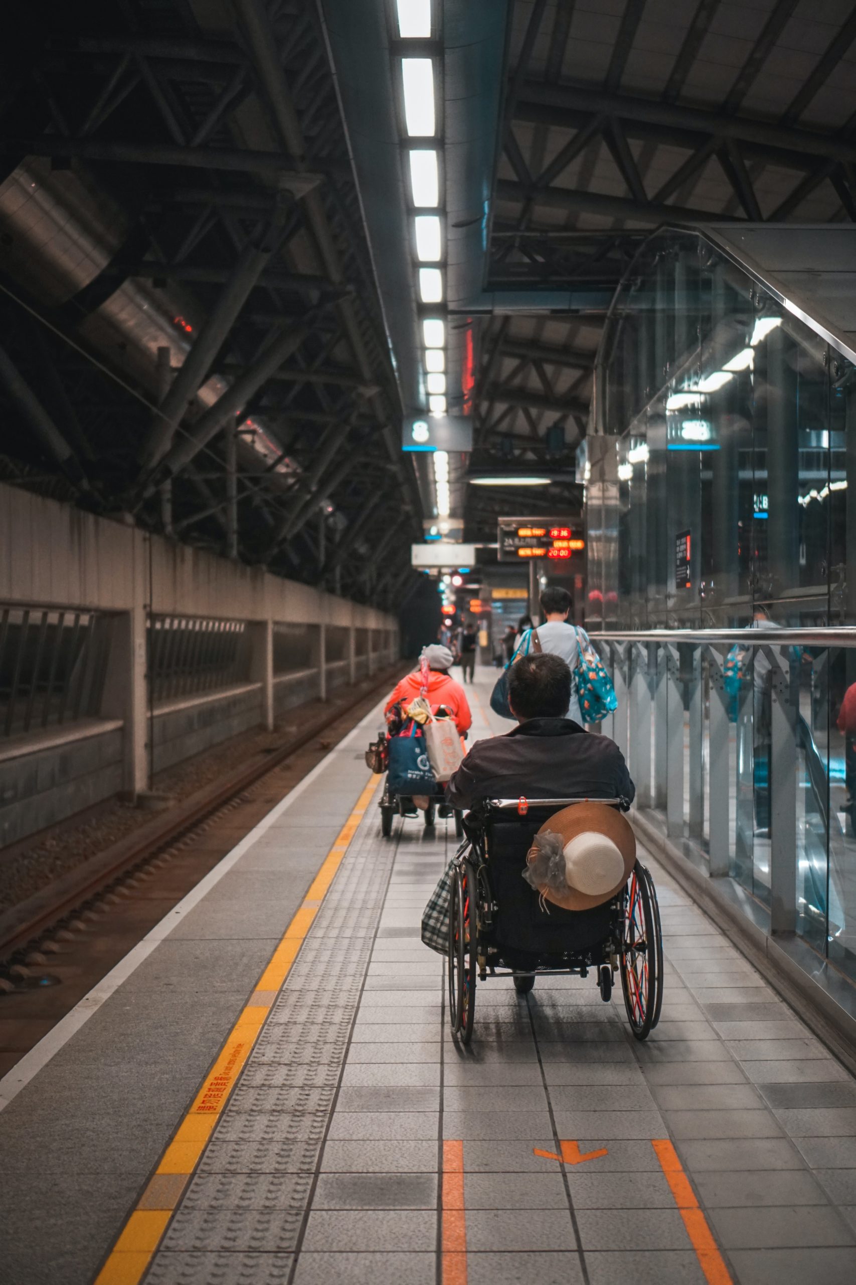 Zwei Rollstuhlfahrer*innen, die an einem Bahnsteig entlang fahren.